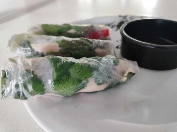 3 Sommerrollen auf einem Teller neben einem schwarzen Schälchen mit Sauce