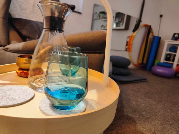 2 türkisfarbene Gläser und eine Wasserflasche auf einem Bestelltisch vor einem Sessel