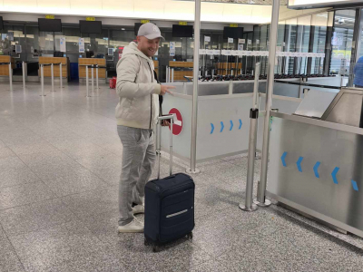 Junger Mann mit Cappy steht mit Rollkoffer vor der Abfertigung am Flughafen. 